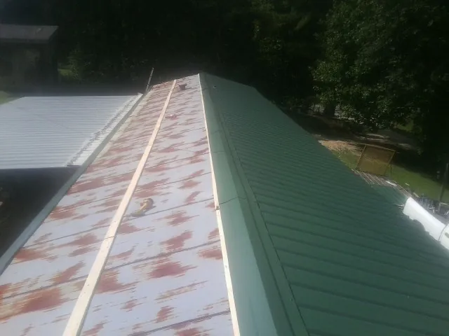 Old rusted panels beside newly installed green metal roofing — Wind Damage Roof Repair by Roofing Brothers in Russell