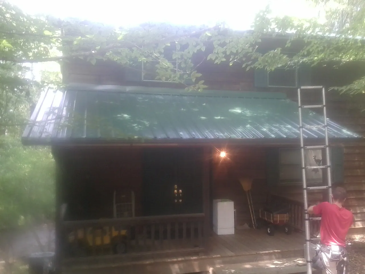 Worker on a ladder at the green porch roof of a wooded cabin in Russell